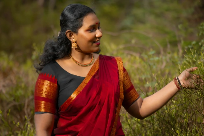Woman in a red sari touching a plant outdoors plant. This shows one of the artists from southern India who works with us and makes thanjavur toys.